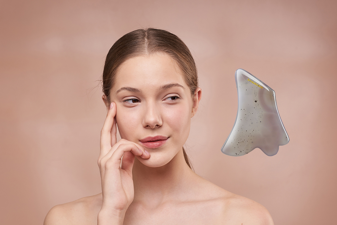 a beautiful young lady is looking at a agate gua sha stone and thinking about a first try of facial gua sha massage