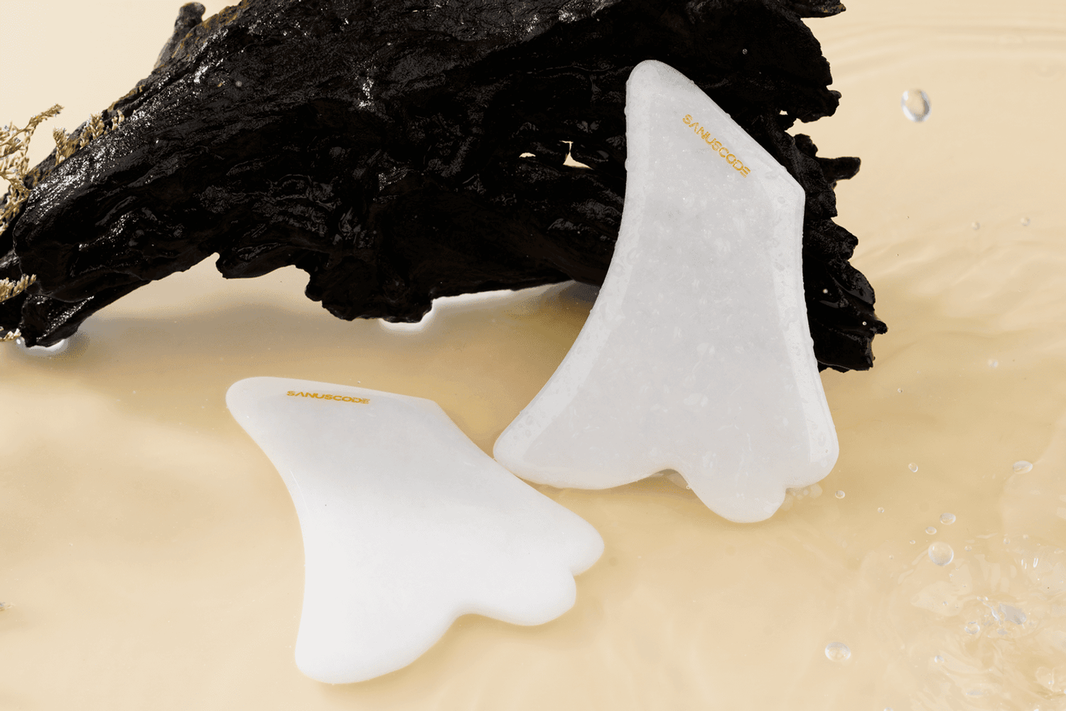 two white jade gua sha stones in front of sandalwood floating in water, beige background
